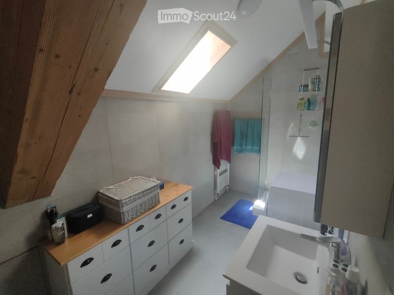 Modern bathroom with a skylight, white tiles, a sink, a mirror, a wooden cabinet, a wicker basket, a towel, a bathtub, and a shower area.