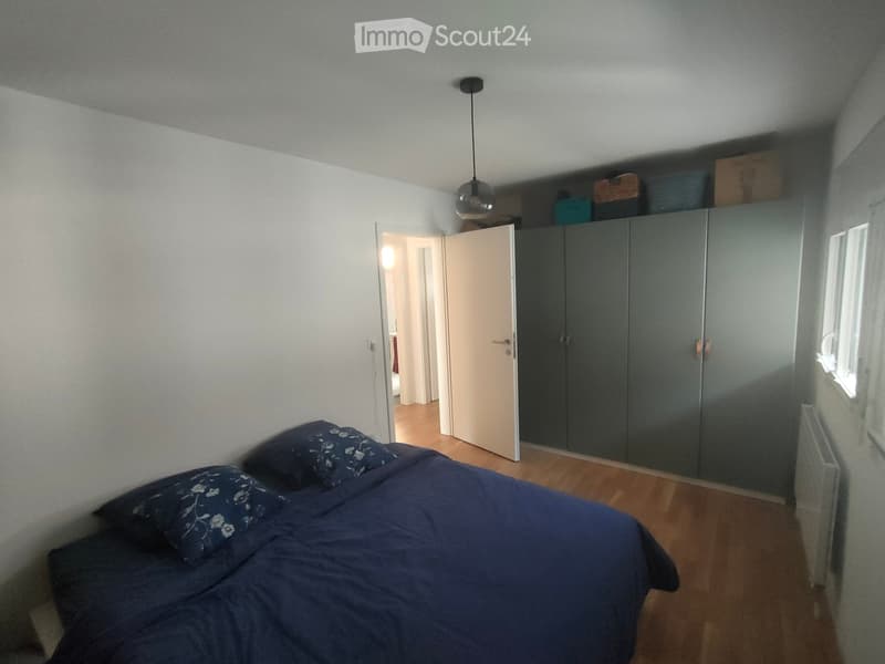 Bedroom with a double bed, pillows, a wardrobe, and a radiator. The room has wooden flooring and white walls.