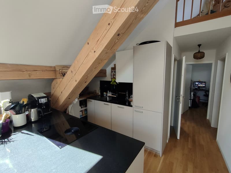 Modern kitchen with white cabinets, black countertops, and a coffee maker on the counter. A wooden staircase leads to an upper level.