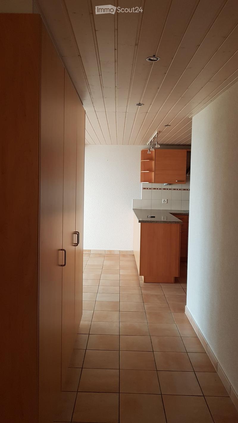 Empty hallway with tiled floor, white walls, and a small kitchen area visible at the end.
