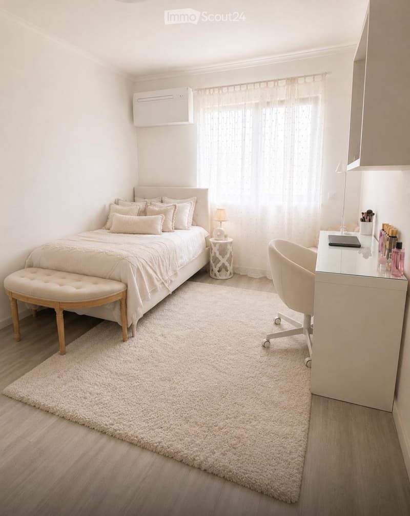 A modern bedroom with a neatly made bed, a bench at the foot, a desk with a chair, a small table lamp, and a large window with sheer curtains.