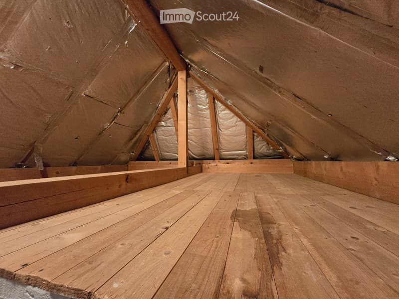 Empty attic space with wooden flooring and exposed wooden beams, insulation visible on the walls and ceiling.