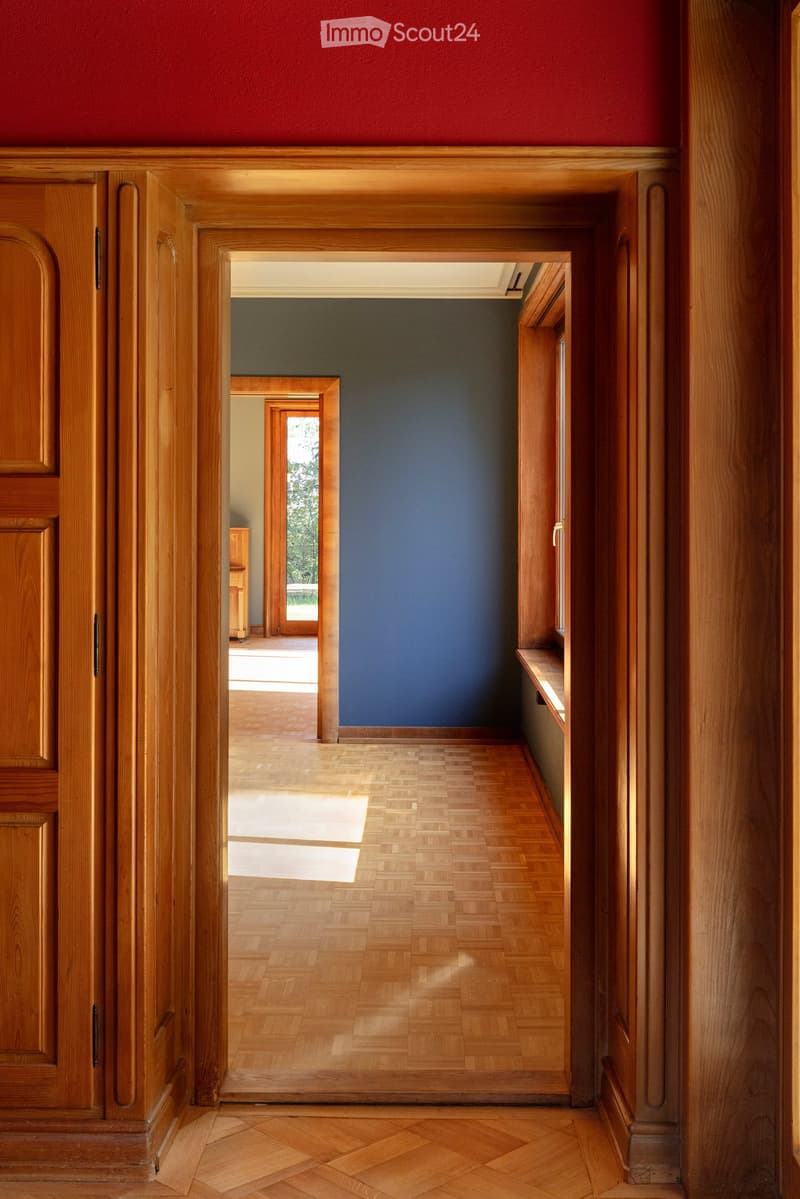 Elegant hallway with wooden flooring, dark blue accent wall, and multiple doorways leading to other rooms.