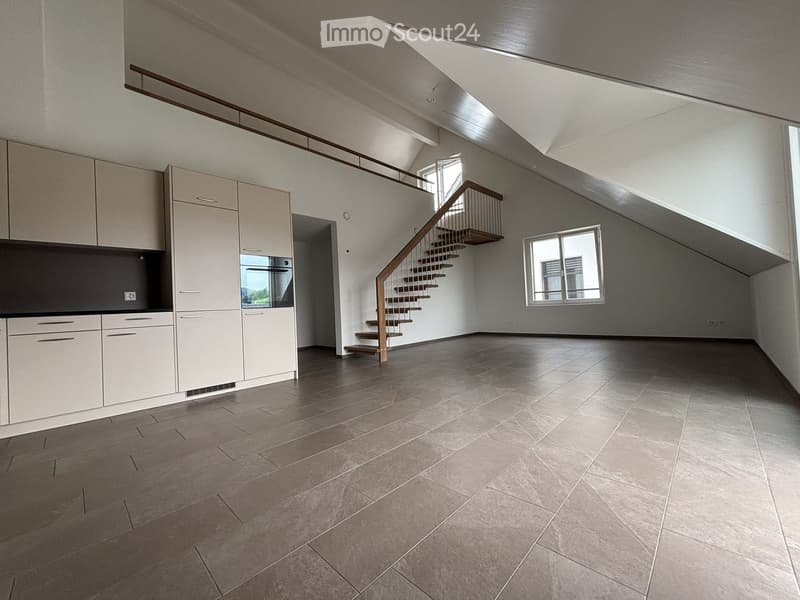 Empty room with modern kitchen cabinets, a staircase leading to an upper level, and large windows allowing natural light.