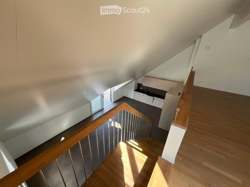 A modern staircase with wooden steps and a metal railing leads down to a kitchen area with white cabinets and a dark countertop.
