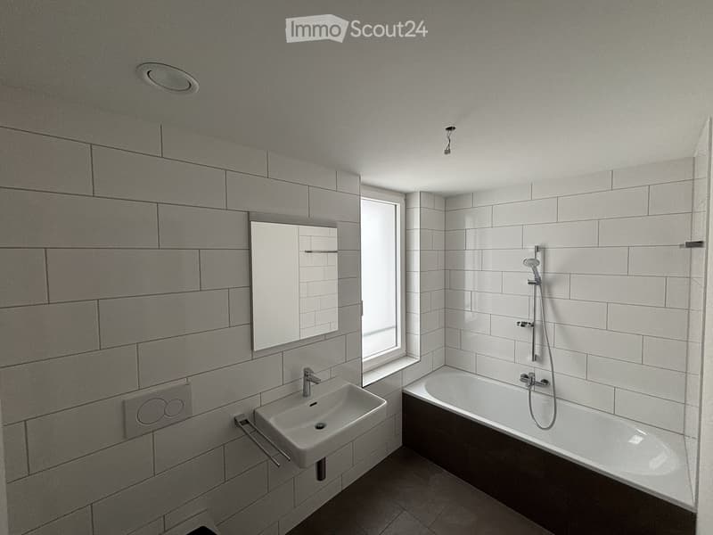 Modern bathroom with white tiles, a sink, bathtub, mirror, and showerhead.