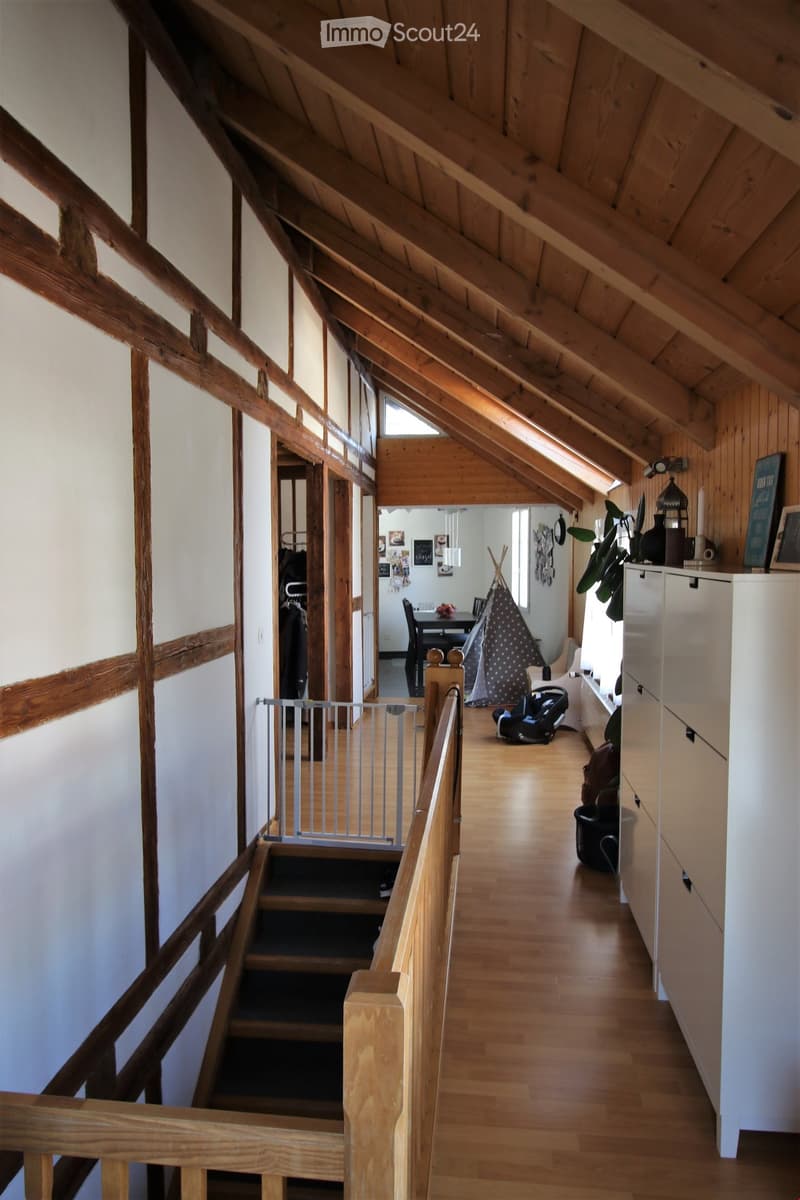 Spacious hallway with wooden floors and exposed wooden beams, leading to a room with a dining table, chairs, and a play tent.