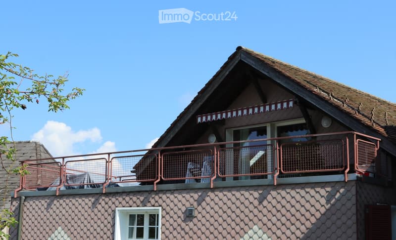A two-story house with a shingled roof, a balcony with metal railings, and a striped awning above the balcony entrance.