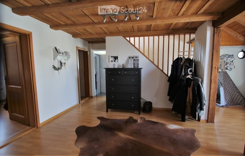 Cozy hallway with wooden floors, exposed wooden beams, a black chest of drawers, coat rack, and a large cowhide rug.
