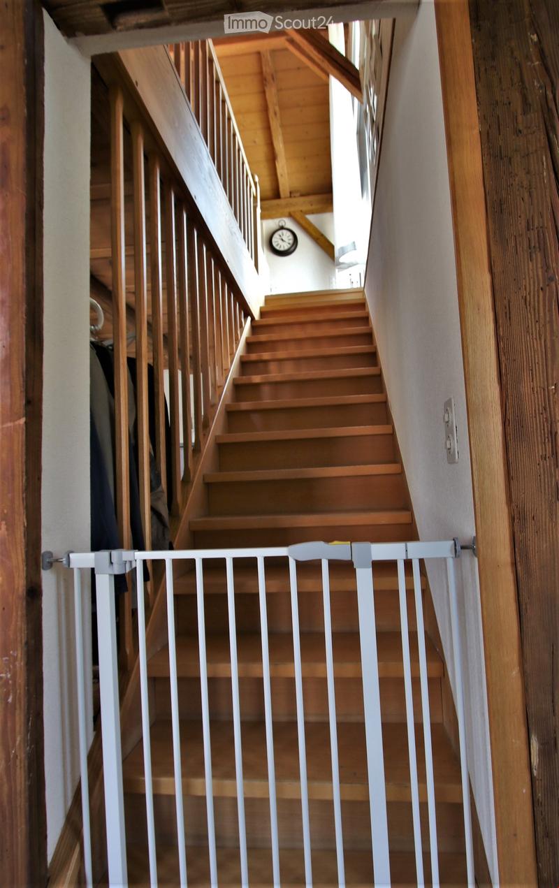 Wooden staircase with a white safety gate, wooden handrails, and a clock on the wall.