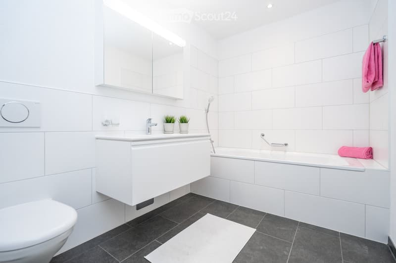 Modern bathroom with white tiles, a white sink, a bathtub, a toilet, a mirror, and a towel on the edge of the bathtub.