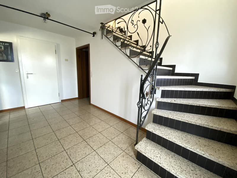 Hallway with tiled floor, white walls, and a staircase with black wrought-iron railing and marble steps.