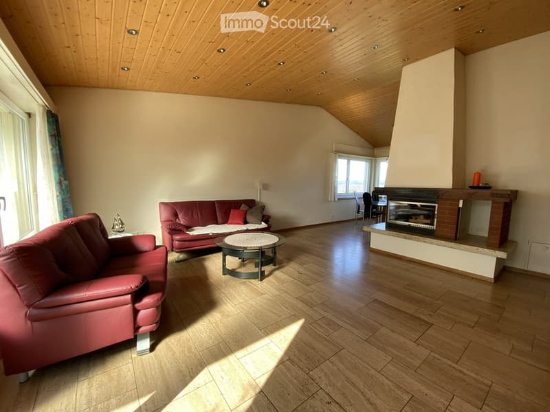 Modern living room with wooden floors, exposed wooden ceiling, fireplace, red leather sofa, coffee table, and large windows.
