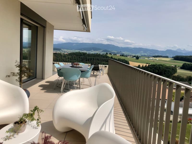 Spacious balcony with a dining table and chairs, overlooking a scenic countryside landscape with mountains in the distance