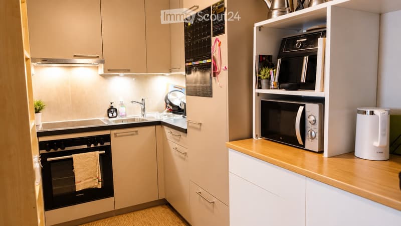 Modern, compact kitchen with light wood cabinets, stainless steel appliances, and a small countertop. Features an oven, microwave, sink, and electric kettle.