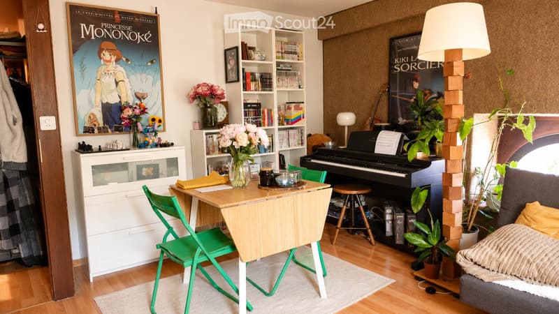A cozy, well-furnished room with a wooden floor, a sofa, a small table with chairs, a bookshelf, a piano, a stool, a flower vase, posters, a lamp, a guitar, and several plants.