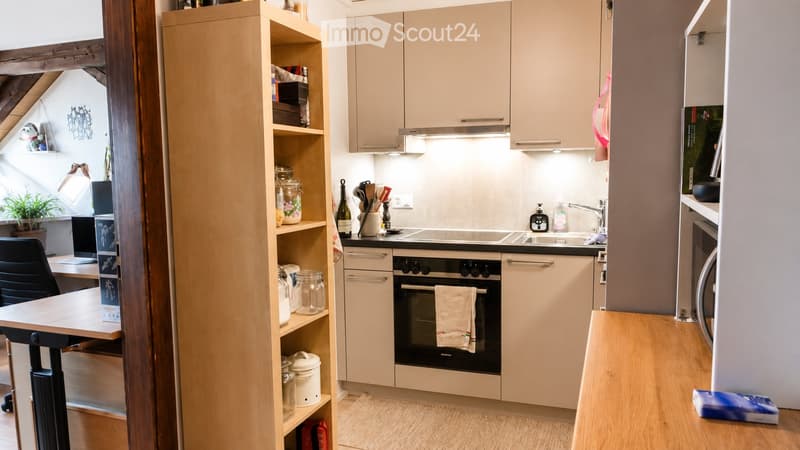 Modern kitchen with light-colored cabinets, stainless steel appliances, and a wooden floor. Includes a built-in oven, sink, and countertop with various kitchen items.
