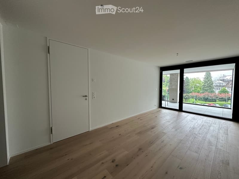 Empty room with light-colored wooden flooring, white walls, and large sliding glass doors leading to an outdoor area.