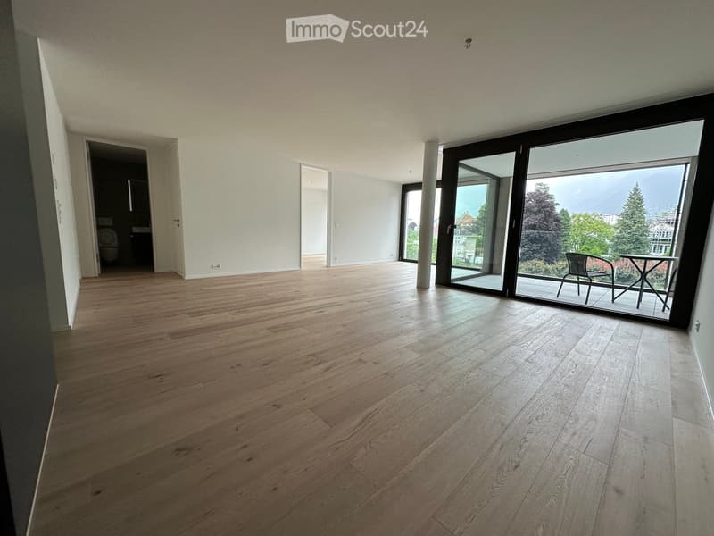 Empty room with wooden flooring, large sliding glass doors leading to a balcony, and a view of greenery outside.