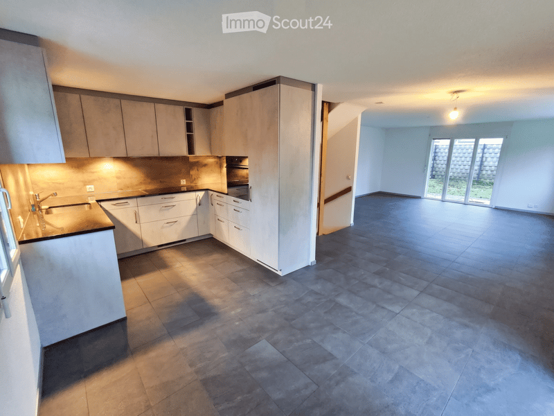 Unfurnished Room. Open-plan space with a modern kitchen area featuring white cabinets, a sink, and a countertop, connected to a large, empty living area with large windows and tiled flooring.