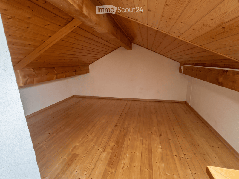 Unfurnished Room. Empty attic space with wooden floors and exposed wooden beams on the ceiling. Light-colored walls and a slanted roof design.
