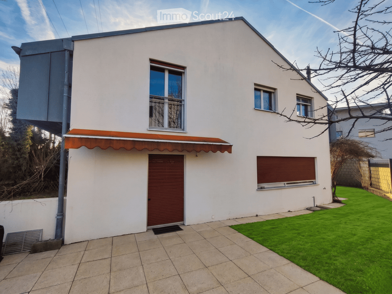 House. Modern single-story house with white exterior, large windows, and a covered entrance. Features a tiled patio and a small lawn area.