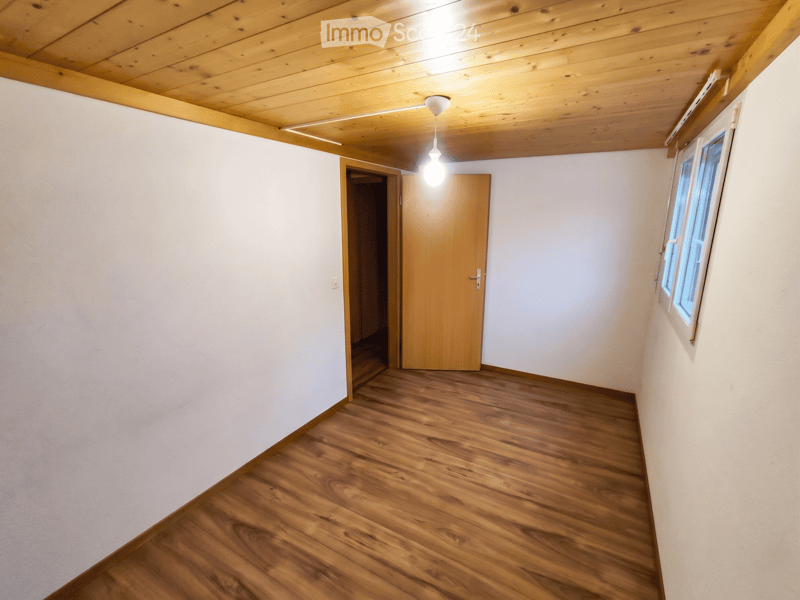 Unfurnished Room. Empty room with wooden flooring, white walls, a single window, and a wooden door leading to another space.