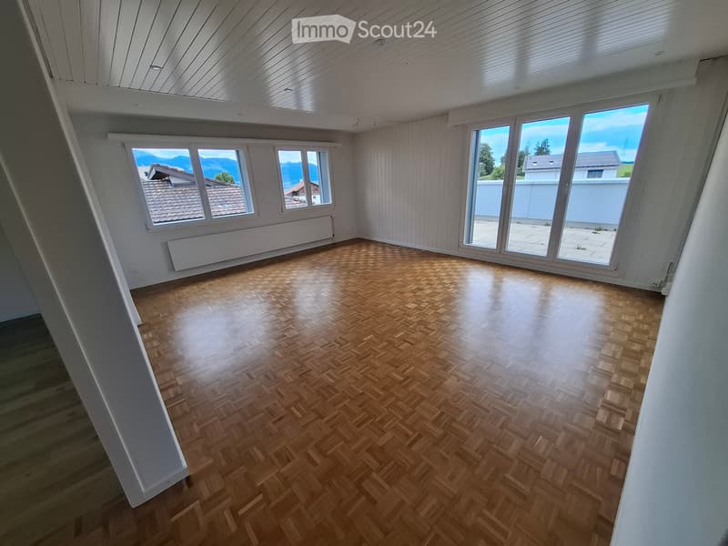 Empty room with wooden parquet flooring, white walls, large windows, and a slanted ceiling.