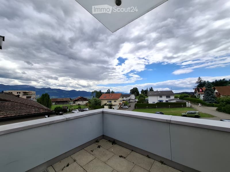 Balcony with tiled floor and white railing, overlooking a suburban neighborhood with houses, trees, and distant mountains.