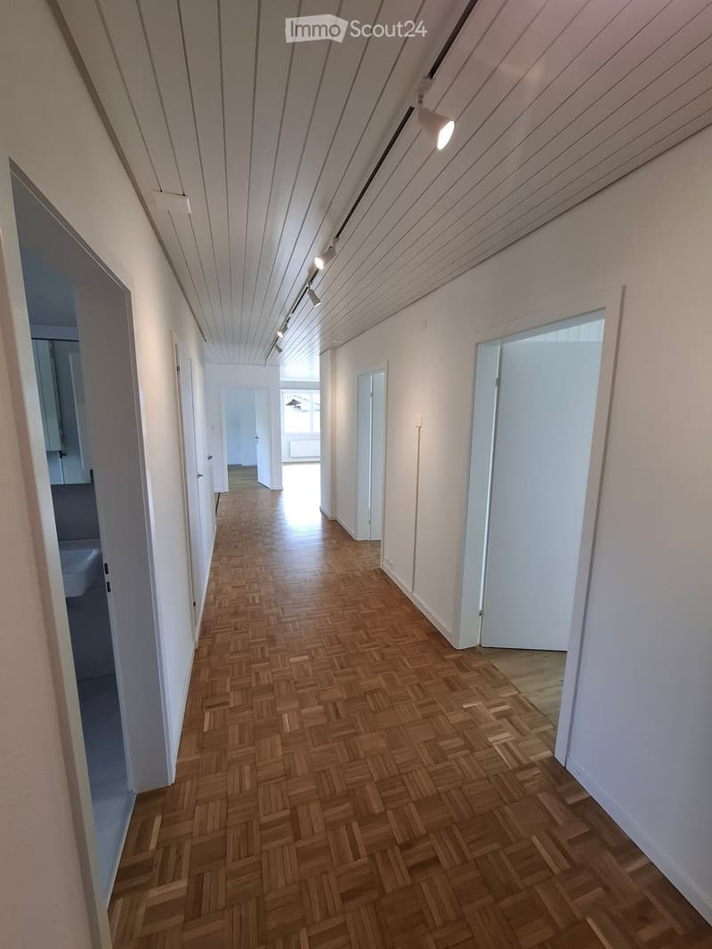 Empty hallway with wooden herringbone flooring, white walls, and recessed lighting. Doors lead to adjacent rooms.