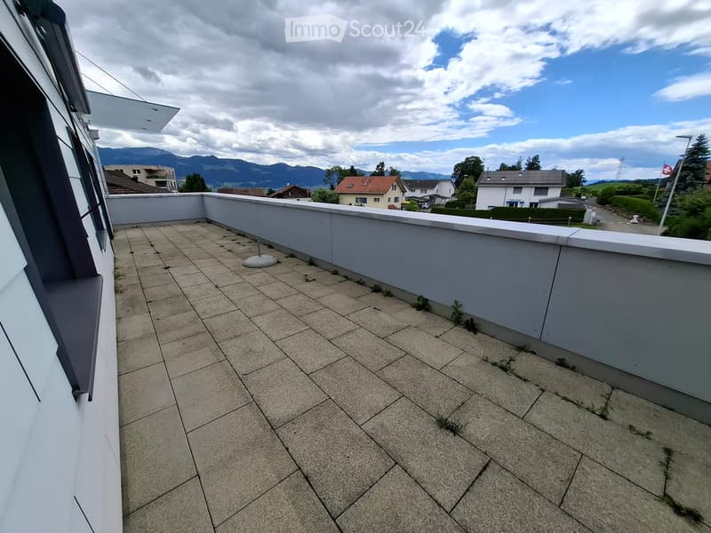 Roof terrace with tiled flooring, low white railing, and distant mountain view.