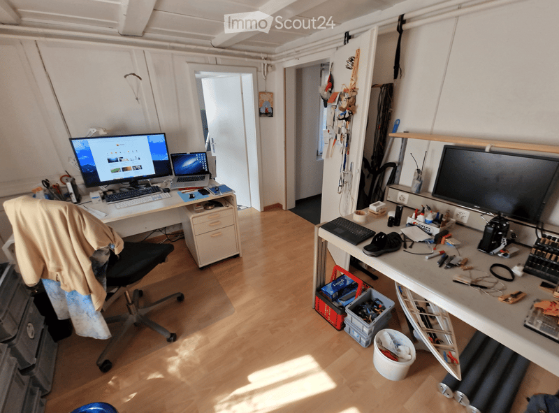 A well-lit room with wooden flooring, two desks, a chair, and various electronic equipment and tools.