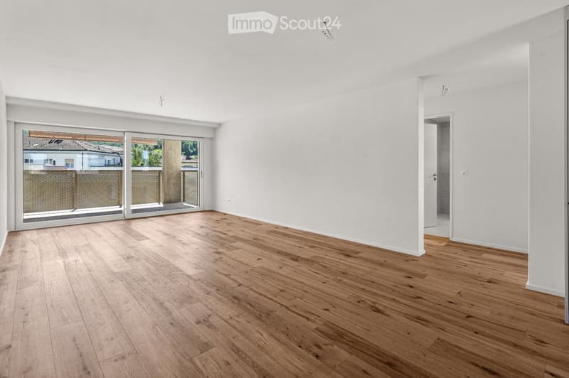 Empty room with light wooden flooring, white walls, and large sliding glass doors leading to a balcony.