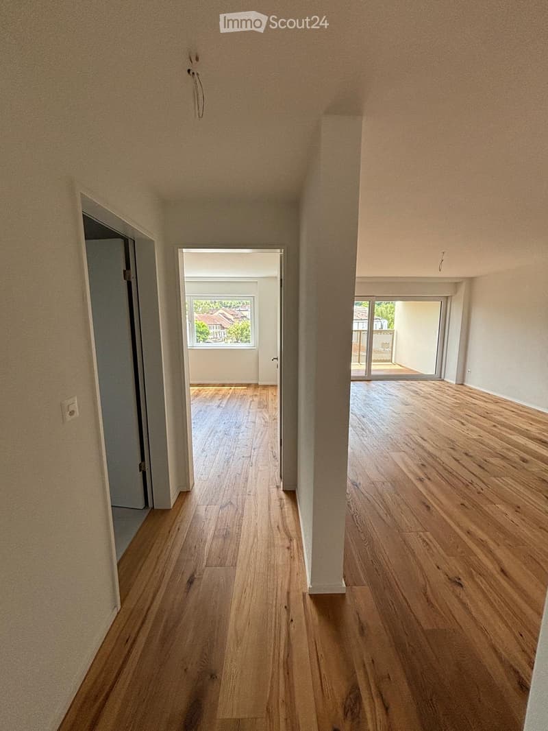 Empty hallway with wooden flooring, beige walls, and multiple doors leading to other rooms and outdoor areas.