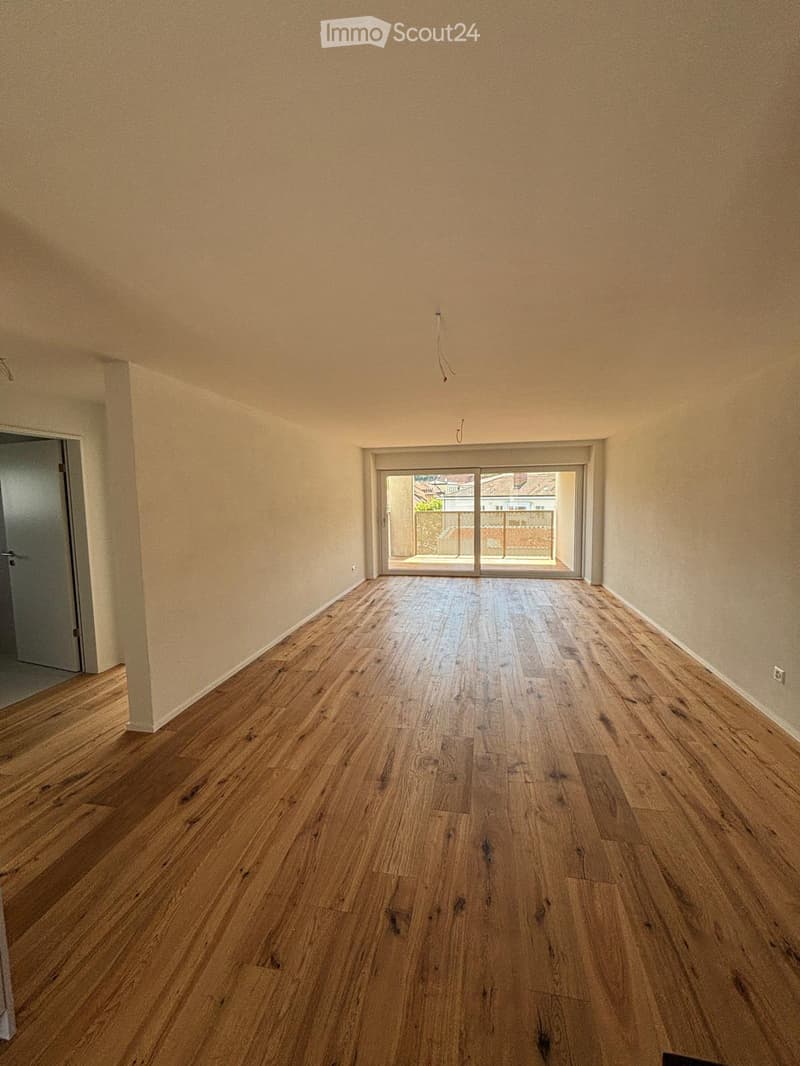 Empty room with wooden flooring, light-colored walls, and a large sliding glass door leading to a balcony.
