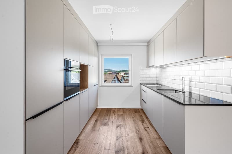 Modern kitchen with white cabinets, wooden flooring, and a large window offering a view of the landscape.