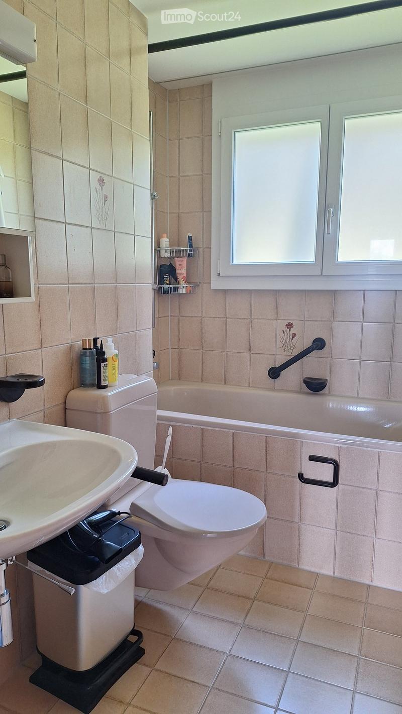Bathroom with beige tiles, a sink, toilet, bathtub, mirror, and handrails for accessibility.