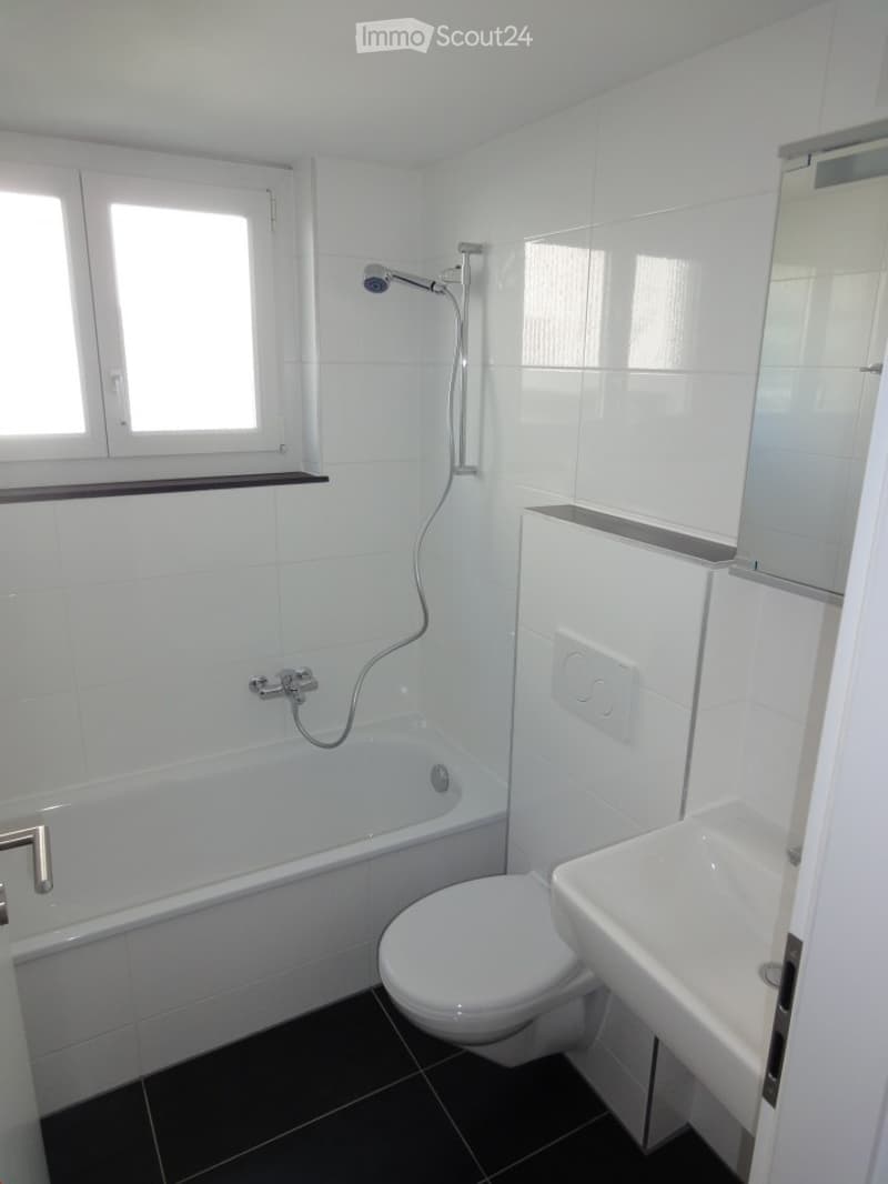 Modern bathroom with white tiles, black floor, bathtub, toilet, sink, and showerhead.