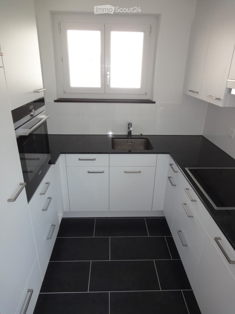 Modern kitchen with white cabinets, black countertops, and black tiled flooring. Features a sink, oven, and stove.