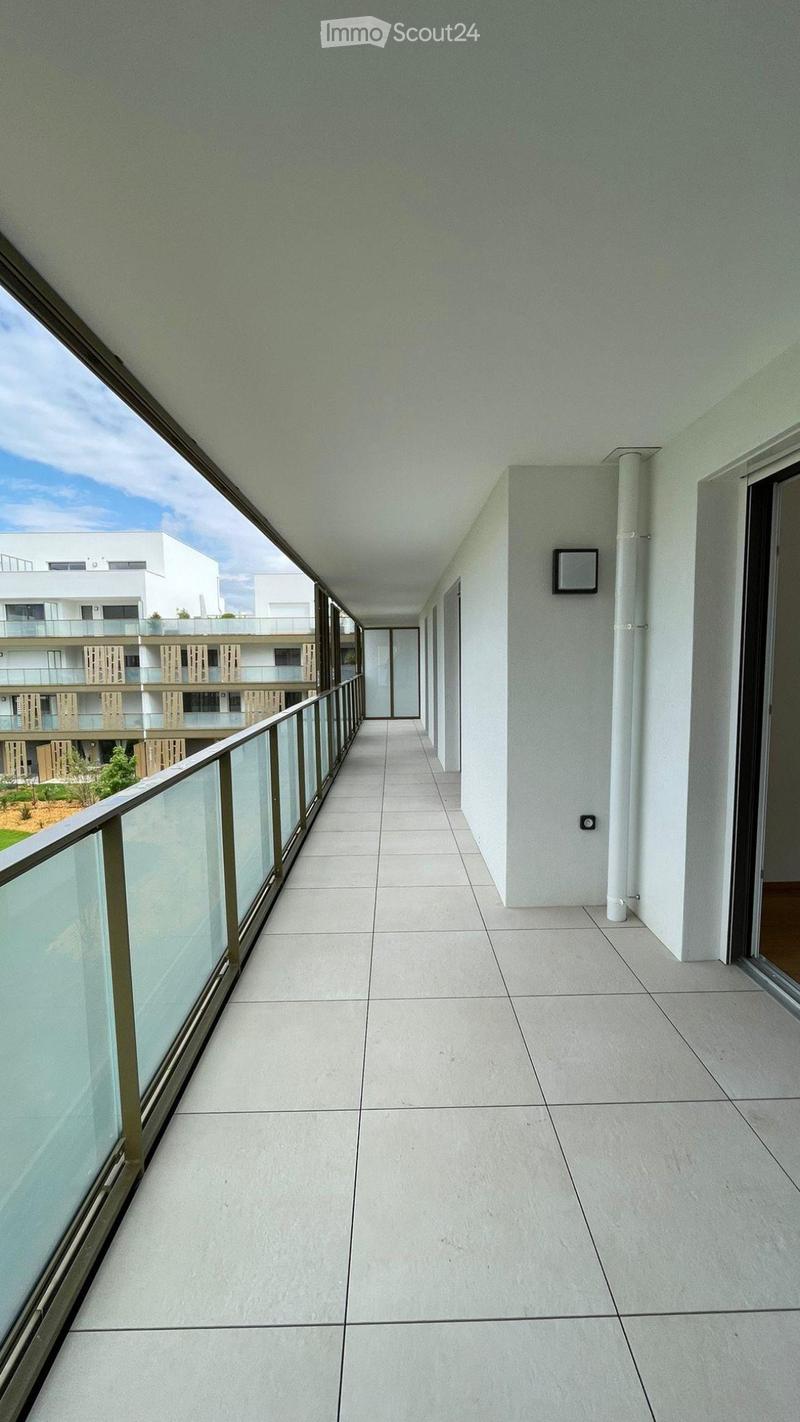 Modern balcony with tiled floor, glass railing, and open view of the building complex.