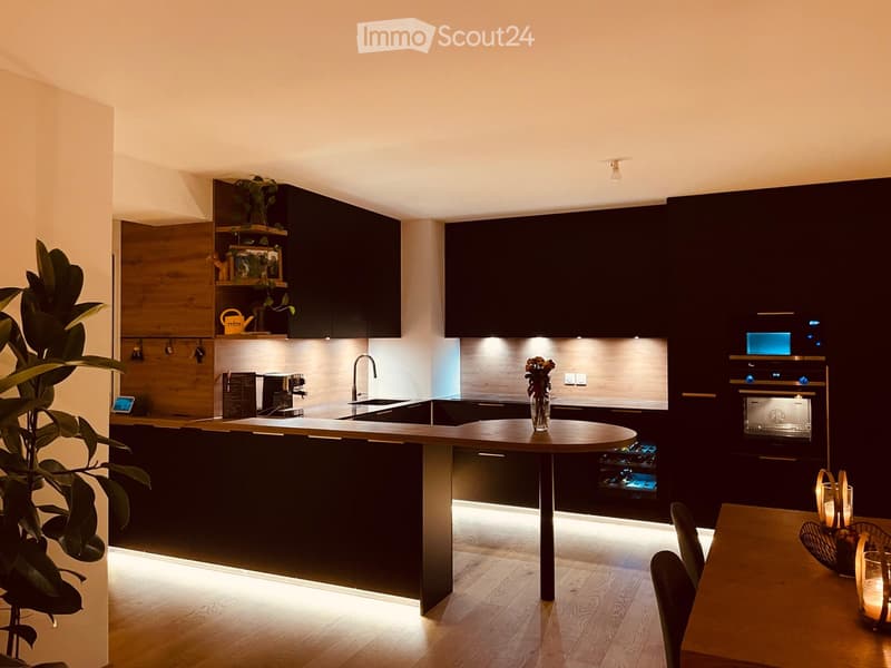Modern kitchen with dark cabinets, wooden island, built-in appliances, and ambient lighting.