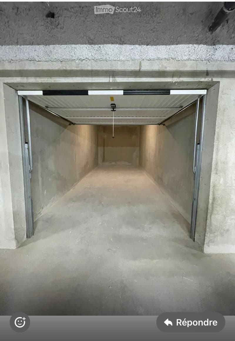 Empty underground garage with concrete walls and ceiling, featuring a partially open metal garage door and a visible ceiling light fixture.