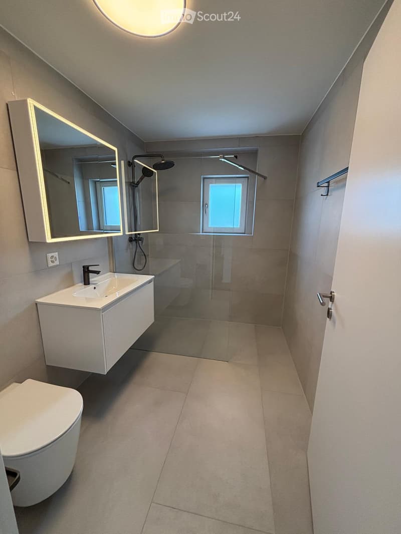Modern bathroom with a white sink, toilet, large mirror, and glass-enclosed shower area.