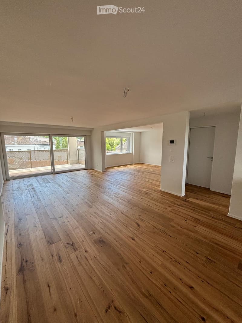 Empty room with wooden flooring, large sliding glass door leading to a balcony, and a window with white frame.