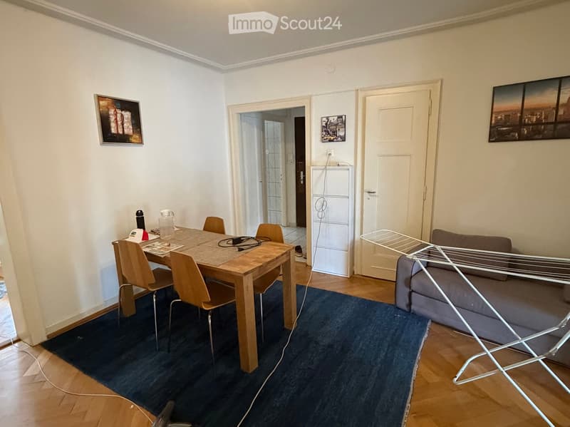 A modern living and dining area with a sofa, a dining table with chairs, a refrigerator, and picture frames on the walls.