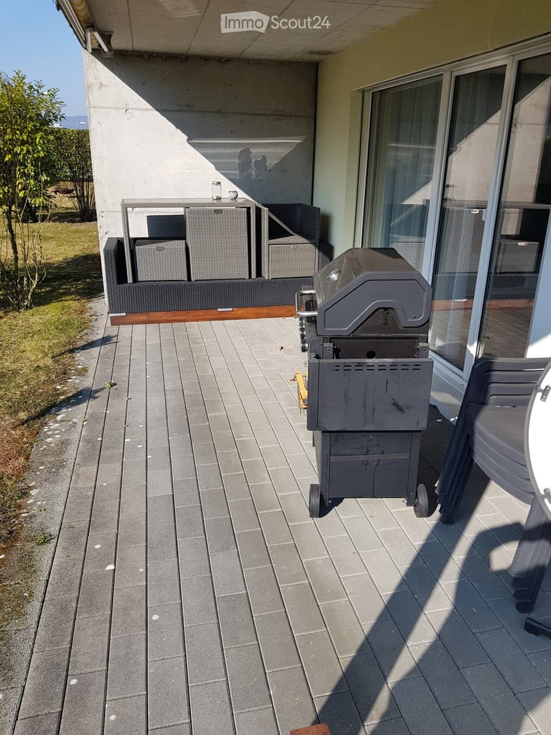 Balcony with tiled floor, barbecue, storage boxes, and a table near the sliding glass door.