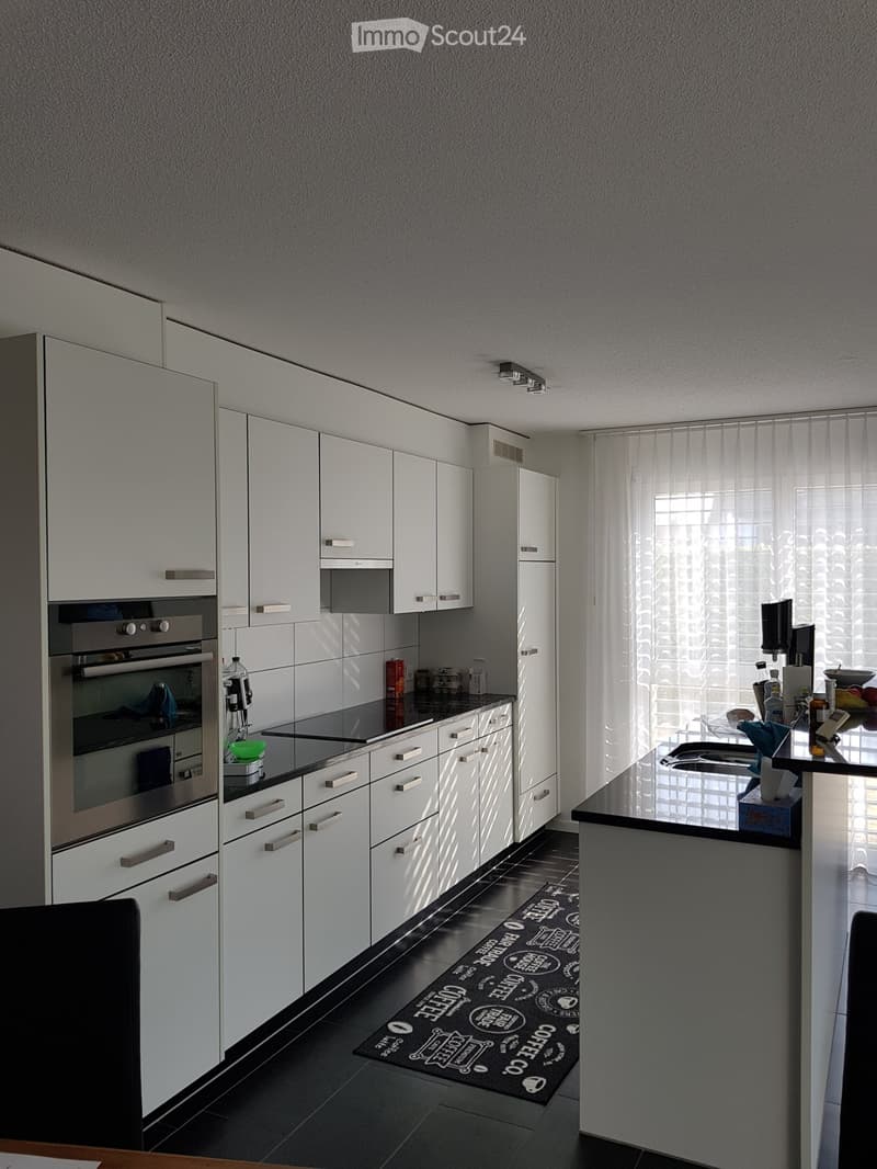 Modern kitchen with white cabinets, stainless steel appliances, and a black countertop. Features an oven, sink, and coffee machine.