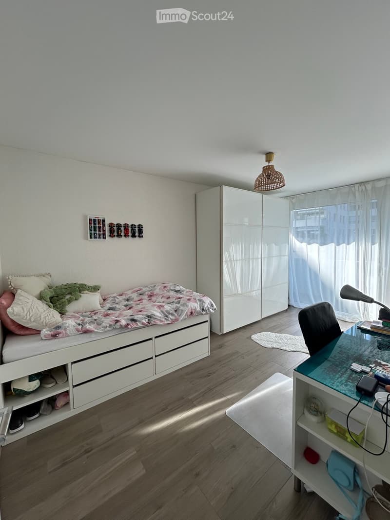 A modern bedroom with a white bed, a large mirror, a desk with a chair, and a hanging lamp.