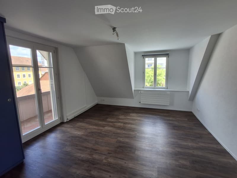 Empty room with wooden flooring, white walls, and large windows, including a sliding glass door leading outside.