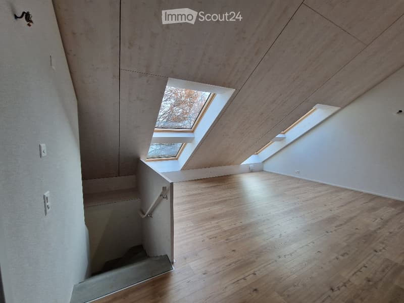 Empty room with wooden flooring, white walls, and skylight windows allowing natural light. Staircase leads to another level.